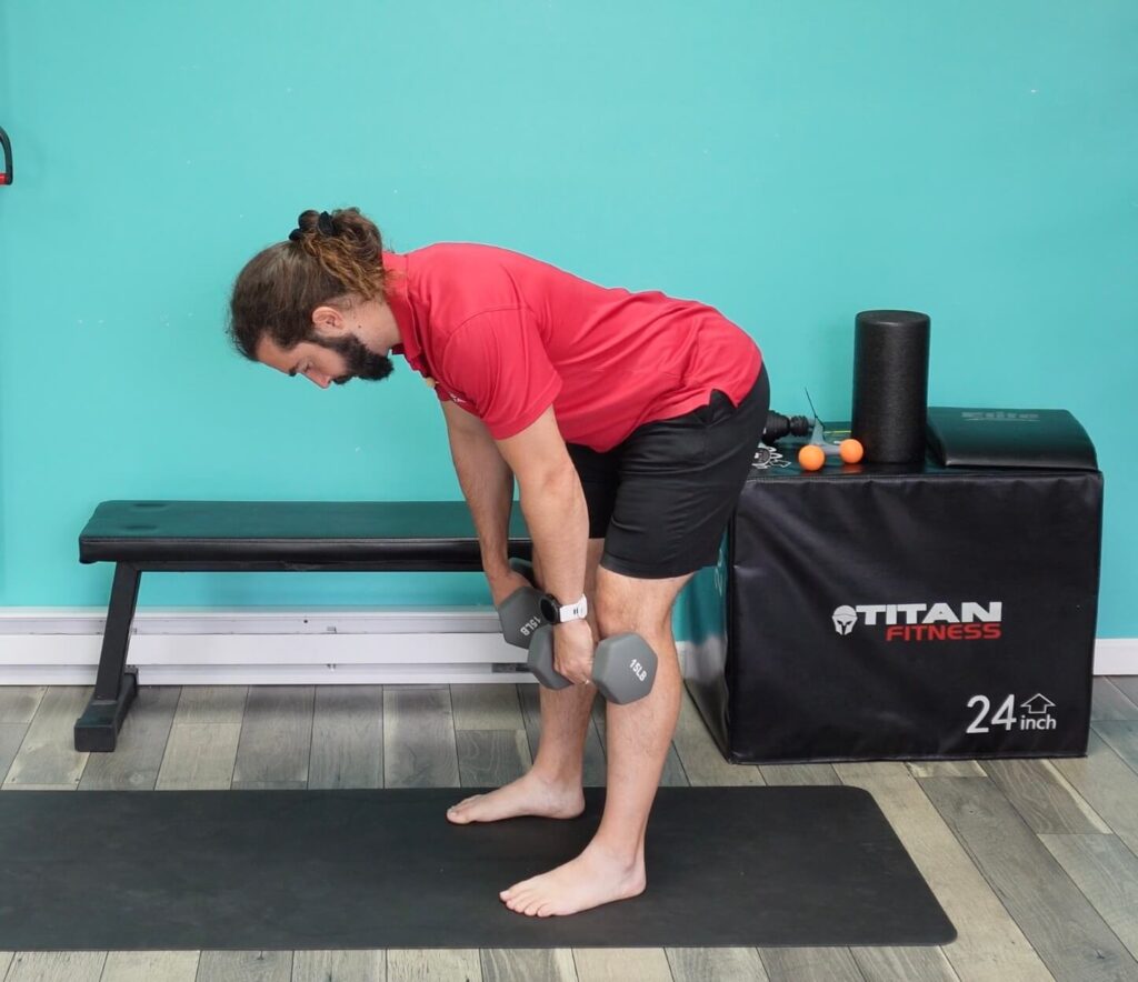 Dr. John improving his hip hinge pattern by pushing his hips back, keeping a straight neutral spine, while holding dumbbells close to his legs to strengthen his lower back